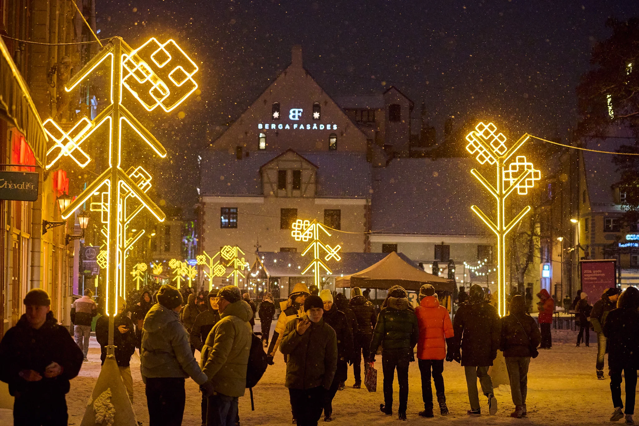 People walking beneath golden festive street lights in Riga